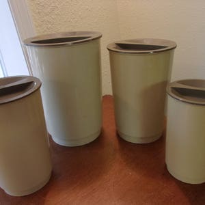 K&ouml;nnte beinhalten: Vier beigefarbene Plastikbeh&auml;lter mit braunen Deckeln. Die Beh&auml;lter sind in verschiedenen Gr&ouml;&szlig;en und in einer Reihe auf einer Holzoberfl&auml;che angeordnet.