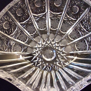 May include: A clear glass bowl with a scalloped edge and intricate star-shaped cutouts. The bowl is designed in a fan shape with a central starburst pattern.