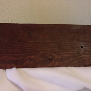 Op de afbeelding: Een donkerbruin houten plank met een glad oppervlak en verschillende kleine gaten. De plank is waarschijnlijk onderdeel van een houten doos of kist.
