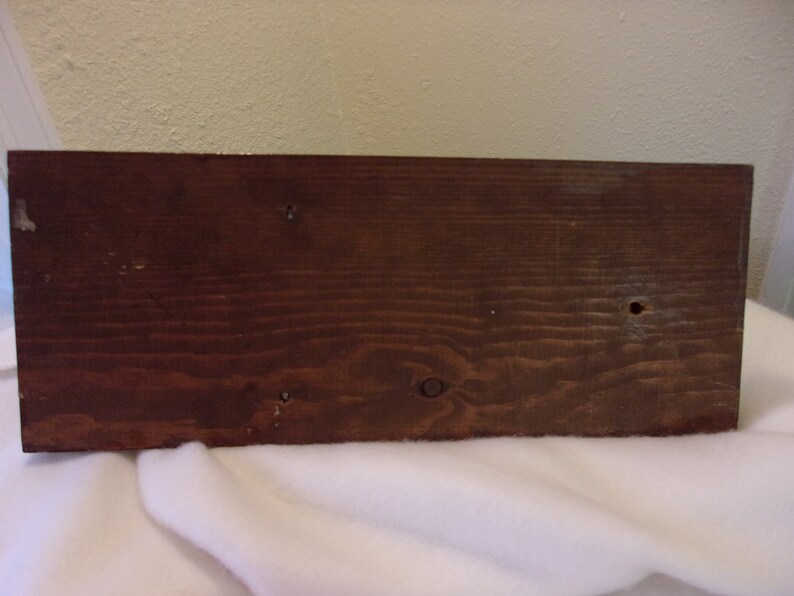 Op de afbeelding: Een donkerbruin houten plank met een glad oppervlak en verschillende kleine gaten. De plank is waarschijnlijk onderdeel van een houten doos of kist.