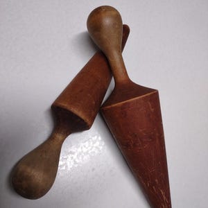 Könnte beinhalten: Zwei antike Küchenwerkzeuge aus Holz. Eines ist dunkelbraun, das andere hellbraun. Beide haben eine konische Form mit einem abgerundeten Griff. Die Werkzeuge werden wahrscheinlich für die Zubereitung von Speisen verwendet.