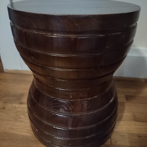 May include: A dark brown wooden stool with a unique stacked design. The stool has a round top and a slightly flared base.