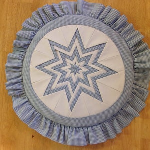 May include: A round blue and white gingham fabric cushion with a white star design in the centre. The cushion has a ruffled edge.