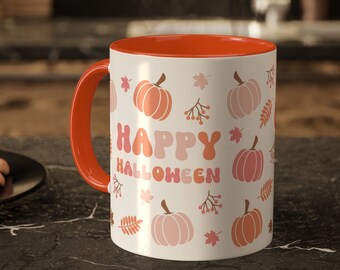 May include: A white ceramic mug with a bright orange handle and interior. The exterior features a repeating pattern of pumpkins, autumn leaves, and berries in shades of orange and pink, with the text HAPPY HALLOWEEN printed in the center.