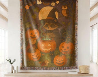 May include: A woven throw blanket featuring a Halloween scene with a raccoon wearing a witch hat, stirring a glowing pumpkin cauldron. The design includes jack-o'-lanterns, a full moon, an owl, bats, and a ghost, finished with fringed edges.