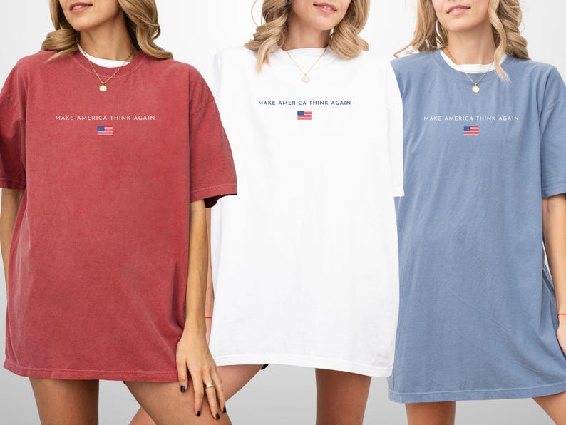 May include: Three oversized t-shirts in red, white, and blue. Each shirt has the text "MAKE AMERICA THINK AGAIN" above a small American flag graphic. The shirts are short-sleeved and have a relaxed fit.