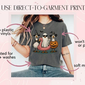 May include: Dark gray t-shirt featuring a Halloween-themed graphic of three ducks dressed as a witch, a ghost, and a jack-o'-lantern. The shirt has the text "WE USE DIRECT-TO-GARMENT PRINTING" and is rated for 75+ washes.