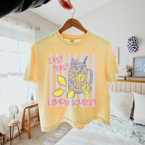Pu&ograve; includere: T-shirt giallo con grafica di limonata, limoni e la scritta "Easy Peasy Lemon Squeezy". La maglietta ha girocollo e maniche corte.