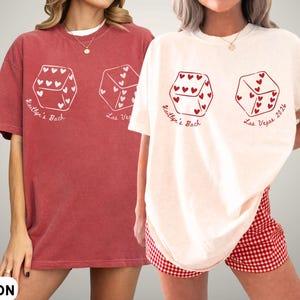 May include: Crimson and ivory-colored t-shirts with a dice graphic. Each die has heart-shaped pips and text that reads "Kaitlyn's Bach" and "Las Vegas 2024". The shirts are oversized and have a casual style.
