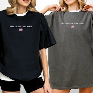 May include: Two oversized t-shirts, one black and one gray, each with the text "MAKE AMERICA THINK AGAIN" and a small American flag graphic. The shirts have short sleeves and a relaxed fit, suitable for casual wear.