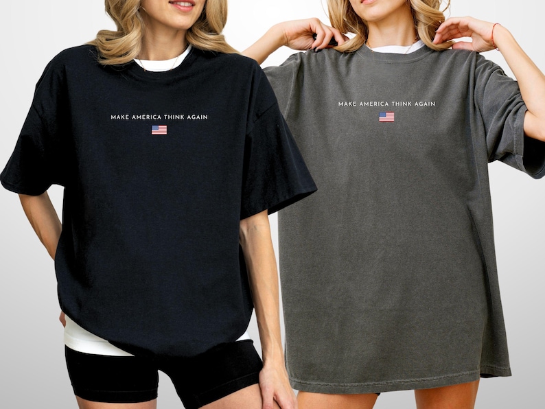 May include: Two oversized t-shirts, one black and one gray, each with the text "MAKE AMERICA THINK AGAIN" and a small American flag graphic. The shirts have short sleeves and a relaxed fit, suitable for casual wear.