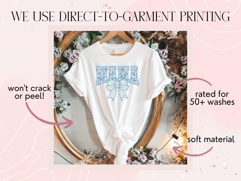 May include: White t-shirt with a blue floral design that says "MAMA" with a blue bow. The shirt is displayed on a gold frame with flowers. The text "WE USE DIRECT-TO-GARMENT PRINTING" is at the top of the image. The text "won't crack or peel!" is on the left side of the image. The text "rated for 50+ washes" is on the right side of the image. The text "soft material" is on the bottom right side of the image.