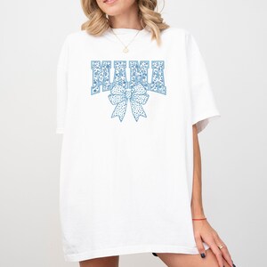 May include: White oversized t-shirt with a blue floral print design that says "MAMA" with a blue floral bow underneath.