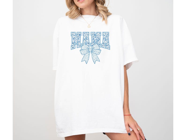 May include: White oversized t-shirt with a blue floral print design that says "MAMA" with a blue floral bow underneath.