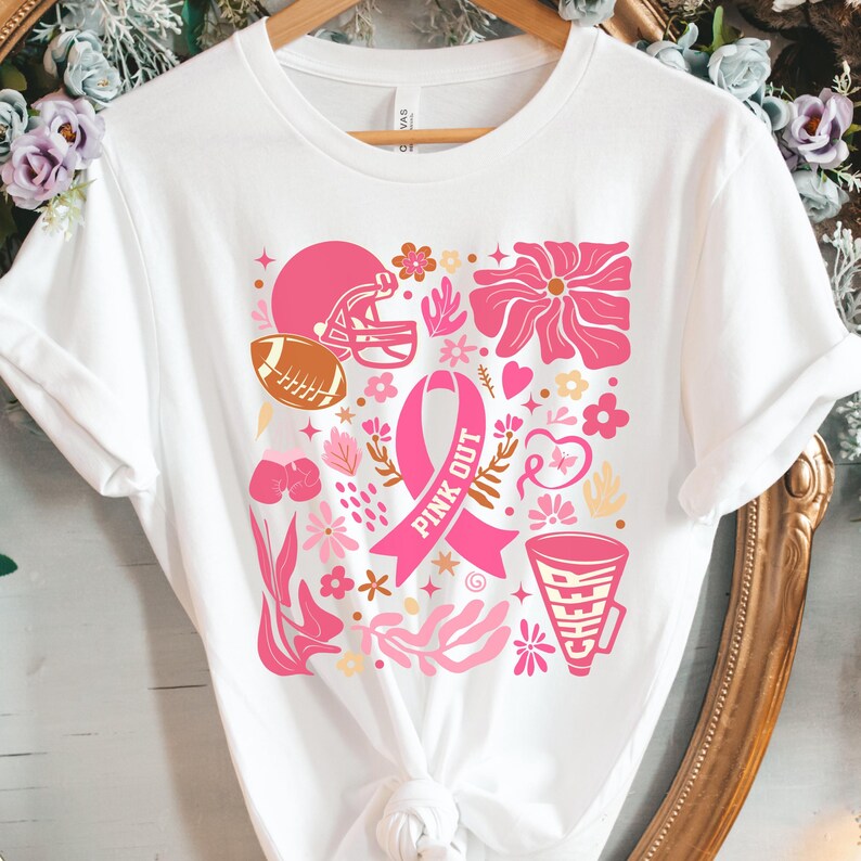 May include: White t-shirt with a pink ribbon, football helmet, and other pink and gold floral designs. The text "Pink Out" is written on the ribbon.
