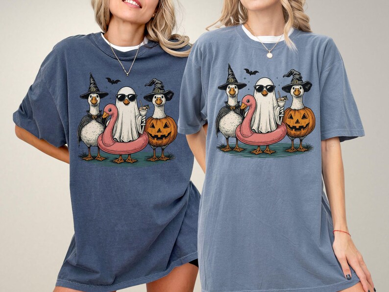 May include: Two blue t-shirts featuring a Halloween-themed graphic. The graphic depicts three cartoon geese dressed in Halloween costumes: a witch, a ghost, and a jack-o'-lantern. A pink flamingo floatie is also included.
