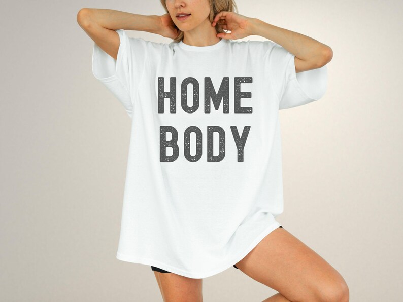 May include: White oversized t-shirt with the text "HOME BODY" printed in black.