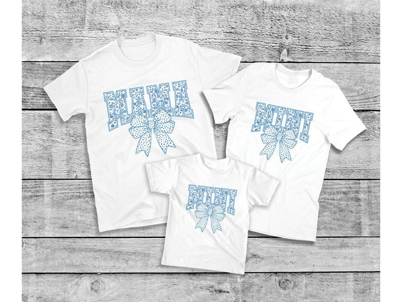 May include: Three white t-shirts with blue patterned text. The largest shirt says "MAMA" with a blue bow. The medium shirt says "MIMI" with a blue bow. The smallest shirt says "MINI" with a blue bow.