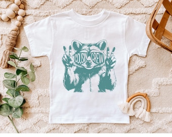 May include: White t-shirt with a teal raccoon wearing sunglasses that say "COUSIN CREW".