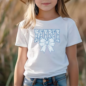May include: A white t-shirt with a blue and white floral pattern design that says "MINI" with a blue and white floral bow.