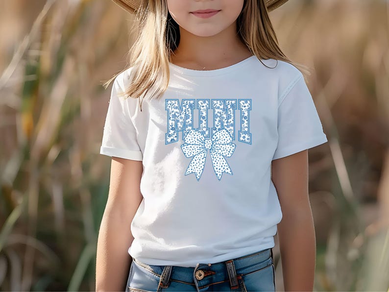 May include: A white t-shirt with a blue and white floral pattern design that says "MINI" with a blue and white floral bow.
