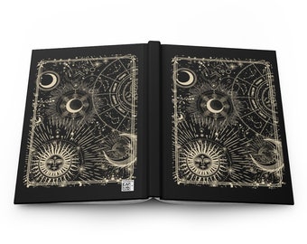 May include: Open black journal with a gold celestial design on the cover. The design features suns, moons, and stars.
