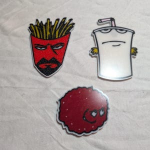 May include: Three cartoon character patches. One is a red french fry container with a black beard and angry eyes. Another is a white milkshake with a straw and arms. The last is a red, round character with white dots.