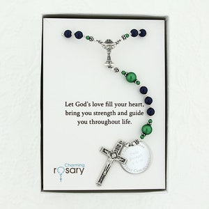 May include: A silver rosary with green and blue beads, a silver chalice charm, a silver crucifix, and a silver round charm with the text "Cola Joseph First Communion". The rosary is in a white box with a card that reads "Let God's love fill your heart, bring you strength and guide you throughout life." and "Charming rosary".
