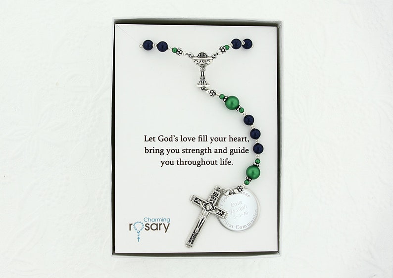 May include: A silver rosary with green and blue beads, a silver chalice charm, a silver crucifix, and a silver round charm with the text "Cola Joseph First Communion". The rosary is in a white box with a card that reads "Let God's love fill your heart, bring you strength and guide you throughout life." and "Charming rosary".