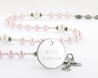 May include: A rosary featuring light pink and white pearl-like beads separated by small silver-toned spacers. A round silver-toned metal pendant is engraved with the name Lily and the date 7-20-24, accompanied by a small silver-toned crucifix charm.