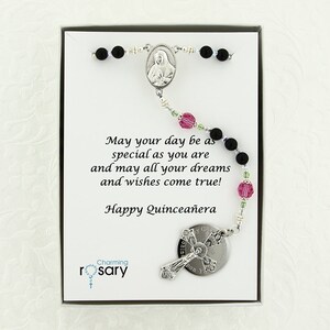 May include: A black and silver rosary with pink and green beads in a white box. The box has a message that reads "May your day be as special as you are and may all your dreams and wishes come true! Happy Quincea&ntilde;era". The box also has the words "Charming rosary" printed on it.