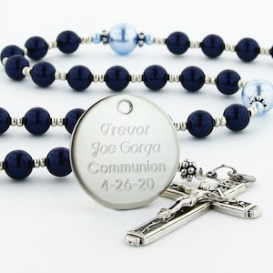 May include: A silver rosary with blue and white beads. The rosary has a silver pendant with the inscription "Trevor Joe Gorga Communion 4-26-20".