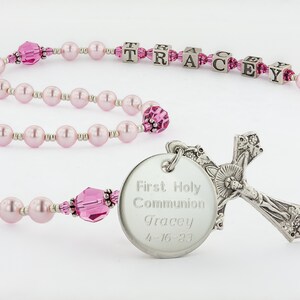 May include: Pink pearl and crystal rosary with a silver cross and a round silver charm engraved with "First Holy Communion Tracey 4-16-23".
