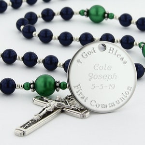 May include: A silver rosary with dark blue and green beads. The center piece is a round silver charm with the inscription "God Bless Cole Joseph 5-5-19 First Communion".