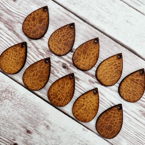 May include: Ten brown leather teardrop-shaped earring blanks with a textured surface.