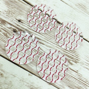 May include: Four clear acrylic ornaments with a baseball pattern. The ornaments are round and have a white background with red baseballs.
