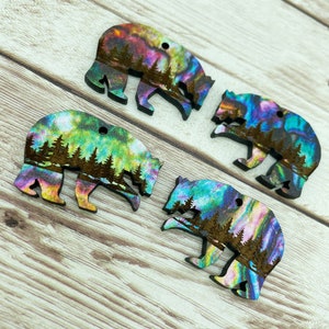 May include: Four wooden bear ornaments with a colorful iridescent finish. The bears are silhouetted against a forest scene.