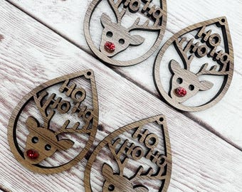 May include: Four wooden teardrop-shaped Christmas ornaments. Each ornament features a reindeer design with the words "HO HO HO" cut out. The reindeer has a red gem for a nose. The ornaments are on a light wood grain surface.