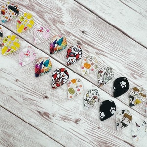 May include: A collection of 16 colorful, clear, teardrop-shaped acrylic earrings with various designs, including pumpkins, chickens, paw prints, and a snowman.