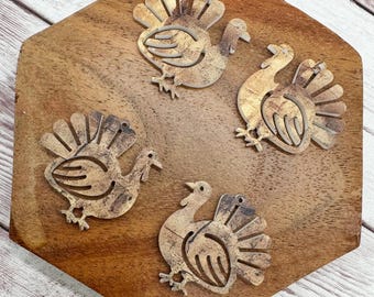 May include: Four wooden turkey cutouts with detailed feather designs, arranged on a wooden hexagonal surface. The turkeys are light brown with darker brown accents, perfect for Thanksgiving or fall-themed crafts and decorations.