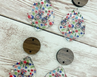 Op de afbeelding: Vier transparante hars oorbellen met een rood, wit en blauw fiets- en bloemenpatroon. Elke oorbel wordt geleverd met een bruine houten cirkel met twee gaten.