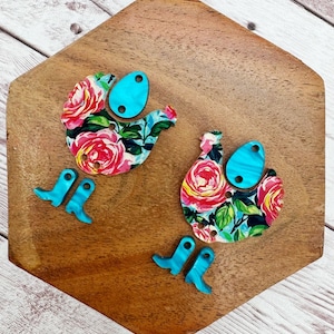 May include: Two wooden chicken cutouts with floral patterns and turquoise accents. The chickens have turquoise boots and eggs.