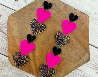 May include: Set of six layered heart-shaped acrylic charms. Each charm features a pink heart layered on top of a leopard print heart. The top layer of each charm is a black heart.