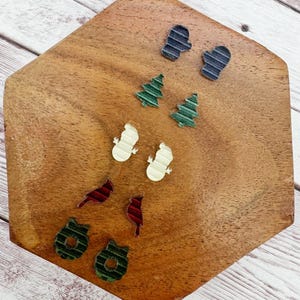 May include: A collection of festive holiday-themed embellishments, including miniature mittens, Christmas trees, snowmen, cardinals, and wreaths. The items are in various colors and textures, arranged on a wooden surface.