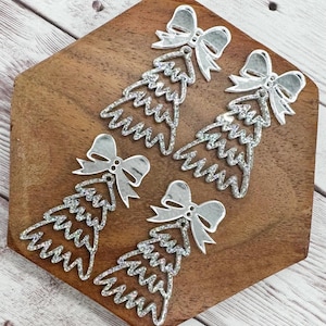 May include: Four silver Christmas tree ornaments with bow accents. The ornaments have a glittery, textured appearance and are arranged on a wooden surface. The bows are smooth and reflective, adding a touch of elegance to the festive decorations.