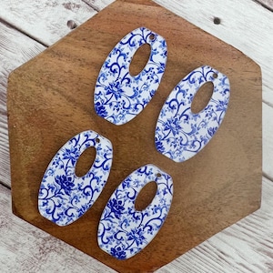 May include: Four blue and white oval-shaped ceramic earrings with a hole in the center. The earrings have a floral pattern.