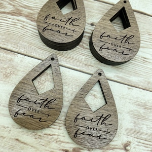 May include: Four wooden teardrop-shaped earrings with a diamond-shaped cutout in the center. Each earring has the phrase "faith over fear" engraved on it.