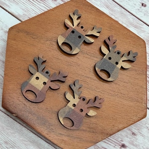 May include: Four flat, reindeer-shaped wooden buttons featuring a brown, tan, and black plaid pattern. Each button has two small holes for attachment and a larger circular cutout at the bottom, showcasing a detailed antler and head silhouette.