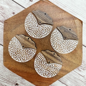 May include: Three white and brown wooden half-circle ornaments with a speckled pattern. The ornaments are arranged on a wooden surface.