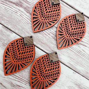 May include: Four orange and brown wooden earrings with a geometric design. The earrings are shaped like a leaf and have a cutout pattern.